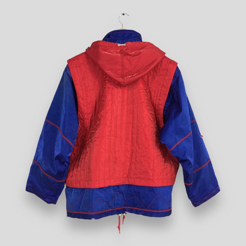 May include: A vintage blue and red jacket with a hood. The jacket has a red center panel with vertical stitching, blue sleeves, and red trim. The jacket is hanging on a hanger.