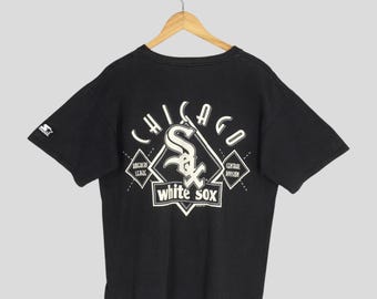 May include: Black vintage Chicago White Sox t-shirt with a white logo on the back. The logo includes the team name, city, and a stylized "S" and "X". The shirt is hanging on a wooden hanger.
