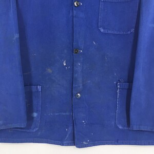 Peut inclure: Gros plan sur une veste de travail bleue avec trois boutons visibles et une poche. La veste pr&eacute;sente des &eacute;claboussures de peinture et des marques d'usure. Fabriqu&eacute;e dans un mat&eacute;riau r&eacute;sistant.
