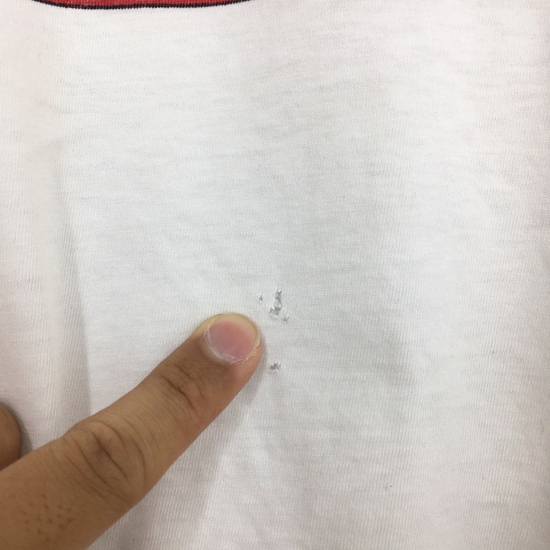 May include: Close-up of a white t-shirt with small holes in the fabric. The holes are visible through the white fabric.