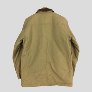 May include: Tan work jacket with a brown corduroy collar. The jacket has a button-up front, long sleeves, and a classic design. The back of the jacket is visible, showing the stitching details and the overall shape. A versatile outerwear piece.