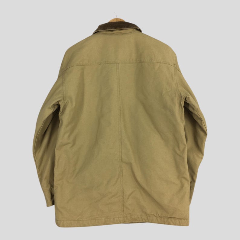 May include: Tan work jacket with a brown corduroy collar. The jacket has a button-up front, long sleeves, and a classic design. The back of the jacket is visible, showing the stitching details and the overall shape. A versatile outerwear piece.