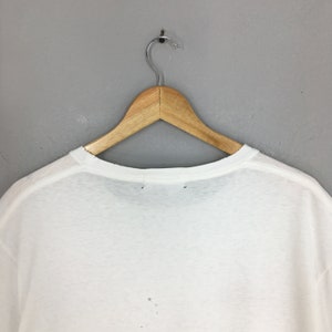 May include: White t-shirt hanging on a wooden hanger against a grey background.