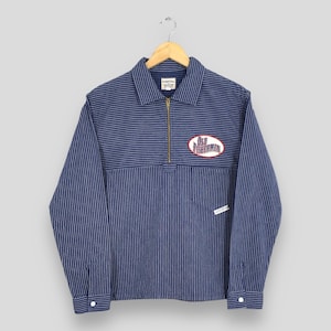 May include: Blue and white striped long-sleeve shirt with a zip-up collar. The shirt features a patch that reads "Old Fisherman" in a red and white oval. The shirt is hanging on a wooden hanger.