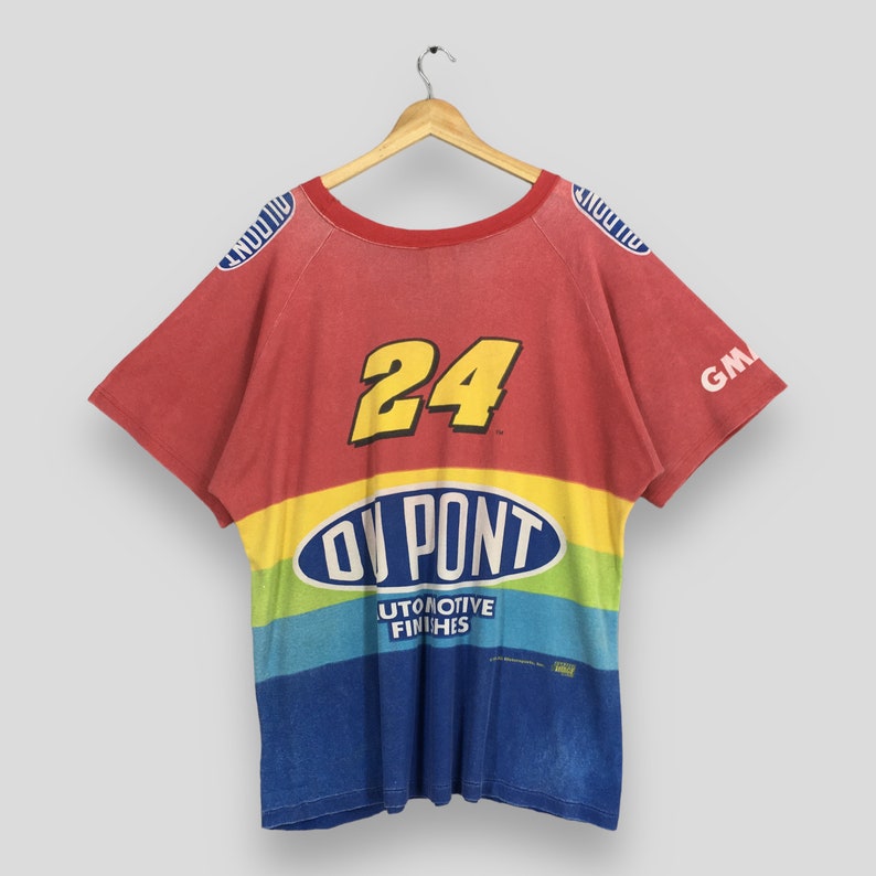 Op de afbeelding: Rood, gele, blauwe en groene t-shirt met korte mouwen en het nummer 24 in geel. Het shirt heeft het logo "DuPont Automotive Finishes" op de borst. Het shirt hangt aan een houten hanger.