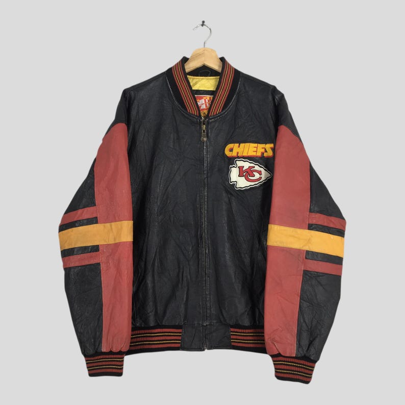 May include: Black bomber jacket with red and yellow detailing. Displays the word "CHIEFS" and a team logo patch on the chest. The jacket has a ribbed collar, cuffs, and waistband. A vintage sports apparel item.