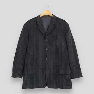 May include: A dark charcoal gray blazer featuring a subtle vertical pinstripe pattern. This garment includes a notched lapel, a four-button front closure, two lower flap pockets, and long sleeves with buttoned cuffs, all displayed on a wooden hanger.