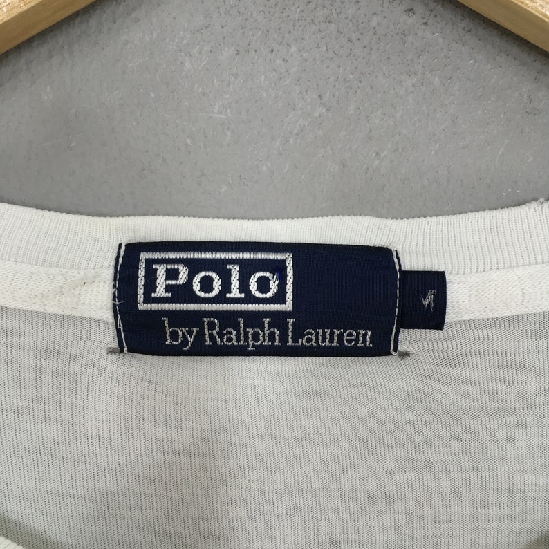 May include: A white Polo by Ralph Lauren tag with blue trim and white text.