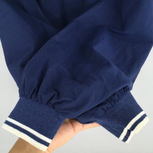 May include: Close-up of the navy blue cuffs of a jacket with white piping. The cuffs are made of a soft, ribbed fabric.