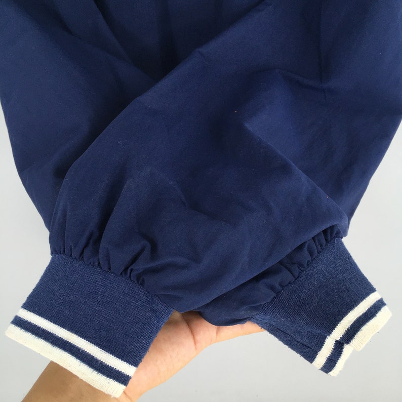 May include: Close-up of the navy blue cuffs of a jacket with white piping. The cuffs are made of a soft, ribbed fabric.