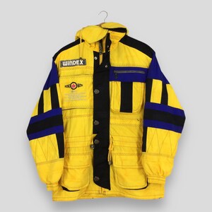 May include: A vintage yellow, black, and blue winter jacket with the word "WINDEX" on the chest. The jacket has a hood, multiple pockets, and a button-up front. The jacket has a retro, sporty design.