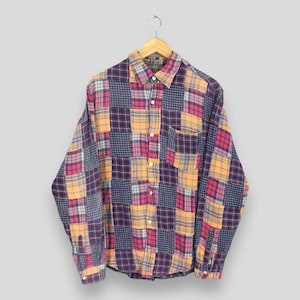 Puede incluir: Una camisa de manga larga con botones y diseño de patchwork. La camisa está hecha de una tela suave y cómoda y presenta una variedad de colores, incluyendo azul, rosa, amarillo y naranja.