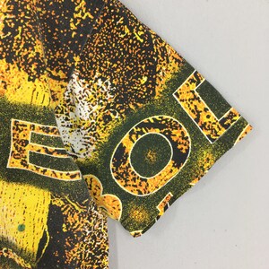 Peut inclure: Gros plan sur un t-shirt &agrave; manches courtes avec un motif abstrait vibrant. Le motif pr&eacute;sente des &eacute;claboussures et des formes jaunes et noires, avec le mot "LOL" en grandes lettres blanches sur la manche. L'esth&eacute;tique g&eacute;n&eacute;rale est audacieuse et accrocheuse.