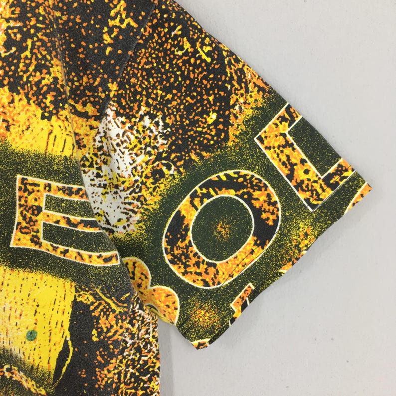 Peut inclure: Gros plan sur un t-shirt &agrave; manches courtes avec un motif abstrait vibrant. Le motif pr&eacute;sente des &eacute;claboussures et des formes jaunes et noires, avec le mot "LOL" en grandes lettres blanches sur la manche. L'esth&eacute;tique g&eacute;n&eacute;rale est audacieuse et accrocheuse.
