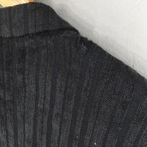May include: A black blazer featuring a vertical ribbed texture and a collared neckline. The fabric displays a distinct linear pattern throughout the garment, with a visible small tear located along the shoulder seam near the collar area.