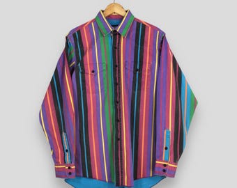 May include: A long-sleeved shirt with vertical stripes in various colors, including purple, red, black, green, and yellow. The shirt has two chest pockets, buttoned cuffs, and a blue lining at the hem. It is hanging on a wooden hanger.