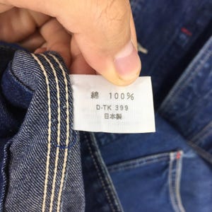 May include: Close-up of a blue denim jacket with a white label sewn into the inside. The label reads "綿 100% D-TK 399 日本製".