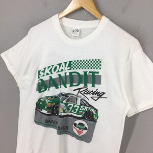 May include: White t-shirt featuring a racing car graphic. The design includes the words "SKOAL BANDIT Racing" in green and black, along with a checkered flag pattern and the number 33 on the car.