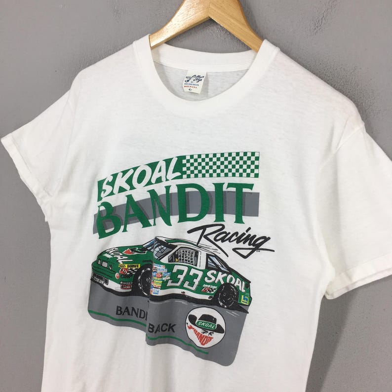 May include: White t-shirt featuring a racing car graphic. The design includes the words "SKOAL BANDIT Racing" in green and black, along with a checkered flag pattern and the number 33 on the car.