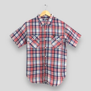 May include: A short-sleeved shirt with a red, white, and blue plaid design. It features two chest pockets and a collar. The shirt is displayed on a wooden hanger.