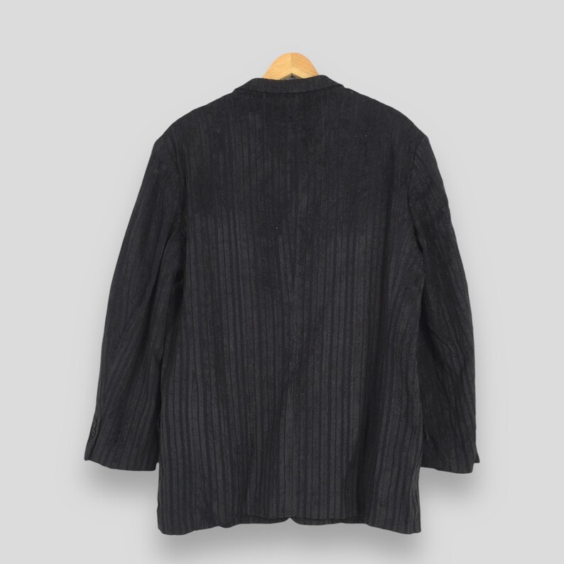 May include: A dark charcoal gray blazer featuring a subtle vertical pinstripe pattern. The garment has long sleeves, a structured collar, and a classic tailored silhouette, presented from a rear-facing perspective against a neutral background.