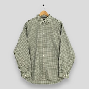 May include: A long-sleeved shirt with a green and white check pattern. The shirt features a button-down collar, a chest pocket, and buttoned cuffs. It is displayed on a wooden hanger.