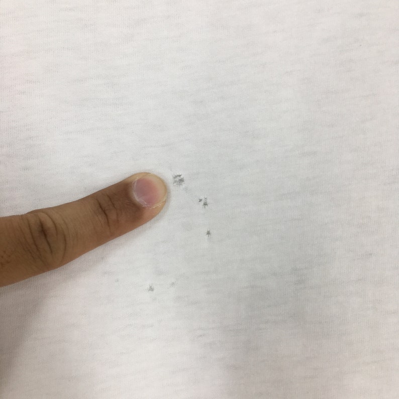 May include: A close-up of a white t-shirt with several small holes in the fabric.