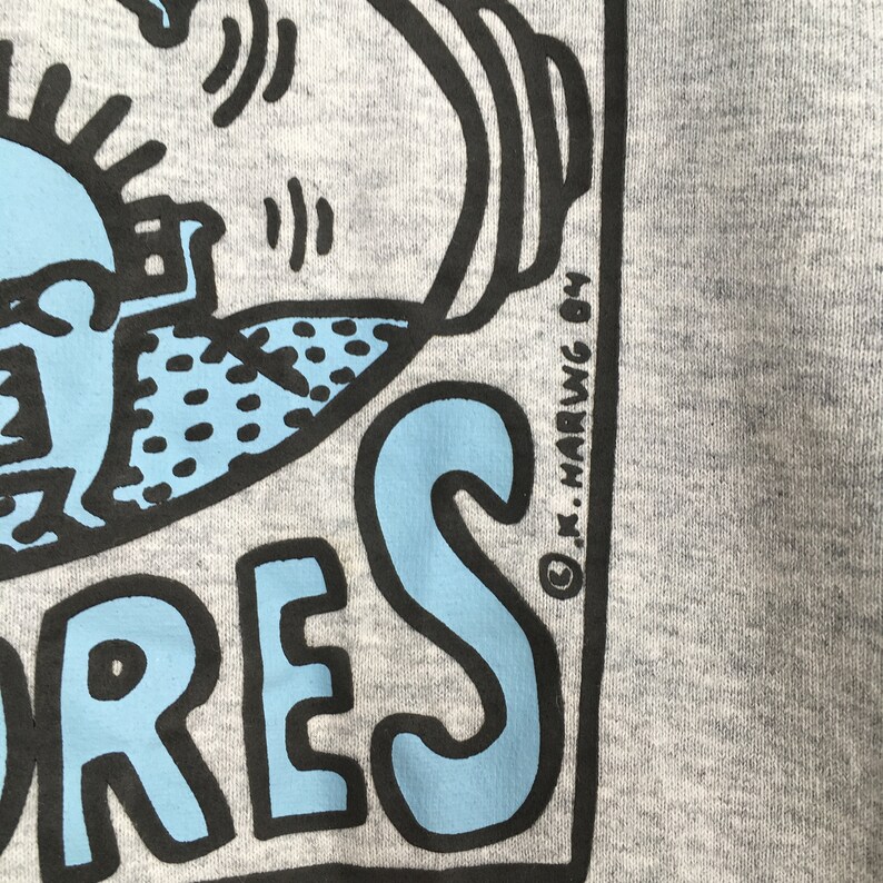 May include: A gray sweatshirt with a blue and black graphic of a person holding a microphone. The text "ORES" is printed in blue and black. The copyright symbol and "K. Haring 84" are printed in black in the bottom right corner.