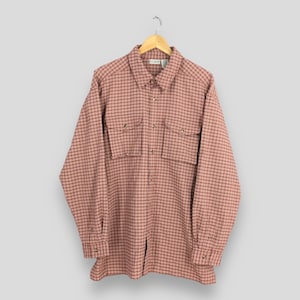 以下が含まれることがあります： 赤と白のチェック柄の長袖シャツ。ボタンダウンで、胸にボタン留めのポケットが2つ付いています。木製のハンガーに吊るされています。柔らかい織り生地で作られています。