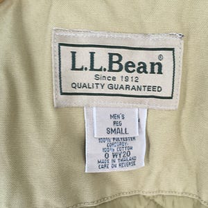 May include: Close-up of an L.L.Bean label, featuring the brand name and "Since 1912 Quality Guaranteed." Below, a smaller tag indicates "MEN'S REG SMALL" and fabric details: 100% polyester corduroy and 100% cotton. The tag also states "MADE IN THAILAND."