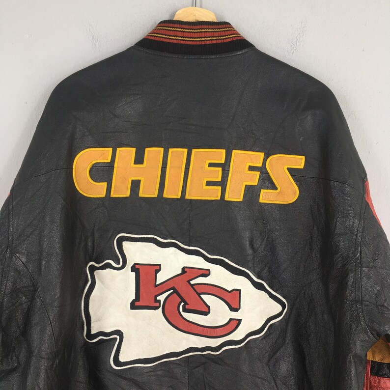 May include: Black leather jacket with the word "CHIEFS" in yellow and orange lettering on the back. The jacket also features the team's logo, a white arrowhead with a red "KC" inside.