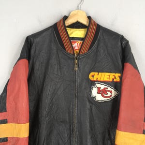 May include: Black leather jacket with red and yellow detailing. The jacket displays the word "CHIEFS" and a team logo patch. It has a ribbed collar with red, yellow, and black stripes.