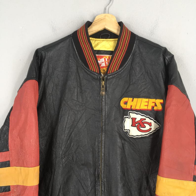 May include: Black leather jacket with red and yellow detailing. The jacket displays the word "CHIEFS" and a team logo patch. It has a ribbed collar with red, yellow, and black stripes.
