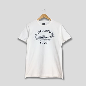 May include: White t-shirt with a navy blue graphic of a ship and the text "U.S.S. YELLOWSTONE AD-27" in a curved font. The shirt is hanging on a wooden hanger against a light gray background.