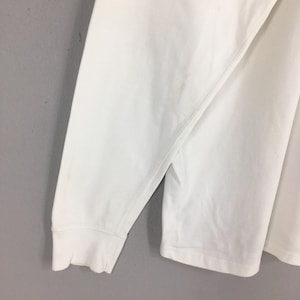 Peut inclure: Gros plan sur une chemise blanche &agrave; manches longues. La manche est visible, avec un poignet c&ocirc;tel&eacute;. Il y a quelques petites taches brun clair sur le tissu. La chemise semble &ecirc;tre faite d'une mati&egrave;re douce, peut-&ecirc;tre du coton.