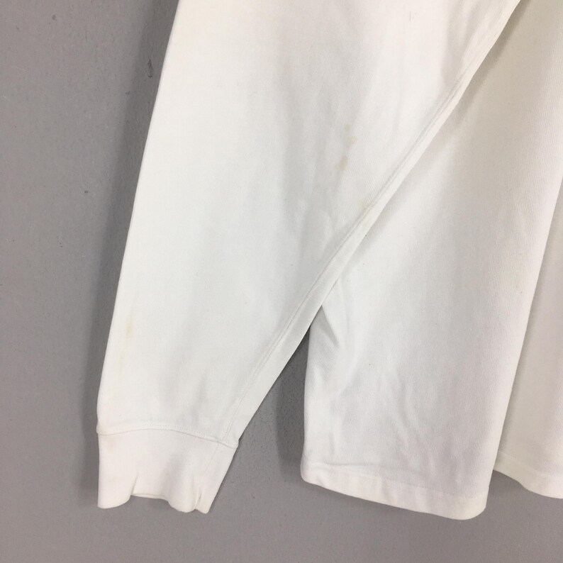 Peut inclure: Gros plan sur une chemise blanche &agrave; manches longues. La manche est visible, avec un poignet c&ocirc;tel&eacute;. Il y a quelques petites taches brun clair sur le tissu. La chemise semble &ecirc;tre faite d'une mati&egrave;re douce, peut-&ecirc;tre du coton.