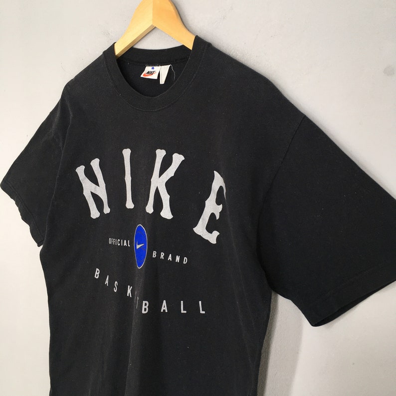 Może przedstawiać: Czarny T-shirt z białym logo Nike i nadrukiem "NIKE OFFICIAL BRAND BASKETBALL" z przodu.