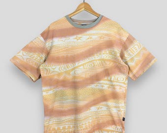 Op de afbeelding: Een T-shirt met korte mouwen met een abstract patroon in perzik- en gele tinten. Het patroon bevat geometrische vormen en sterren.