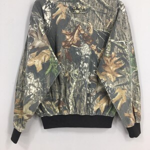 Op de afbeelding: Een sweatshirt met lange mouwen, camouflage-print en een zwarte getailleerde boord. Het sweatshirt heeft het Cabela's logo op de voorkant.