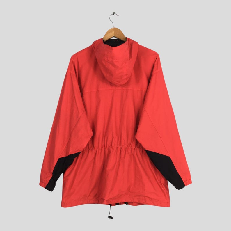 May include: A red hooded jacket with black detailing on the sleeves and a drawstring waist. The jacket is suspended on a wooden hanger. The jacket has a full zip and a hood. The background is light grey.