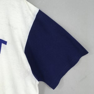 May include: A white t-shirt with a blue sleeve. The shirt has a blue graphic on the front.