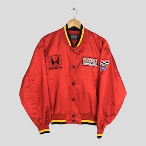 May include: Red satin bomber jacket with a black Honda logo and Target Chip Ganassi Racing patches. The jacket has a black and yellow striped collar and cuffs.