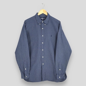 Op de afbeelding: Een marineblauw overhemd met een klein wit ruitpatroon. Het shirt met lange mouwen heeft een button-down kraag en een klein geborduurd logo op de borst. Het shirt hangt aan een houten hanger.
