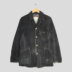 May include: A black denim jacket with a classic design, featuring a collared neckline, button-up front, and multiple pockets. The jacket has gold-colored buttons and a small red tag on the pocket. It is hanging on a wooden hanger.