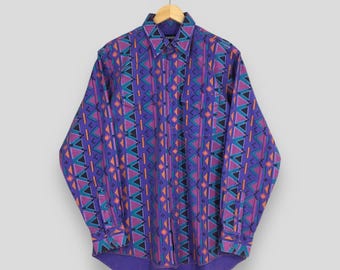May include: A long-sleeved button-down shirt with a vibrant geometric pattern. The shirt features a purple base color with teal, orange, and black triangle and diamond shapes. It has two chest pockets and a classic collar.