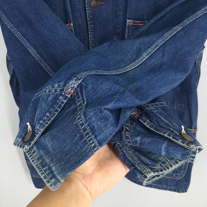 May include: A blue denim jacket with red stitching and a button closure. The jacket has a worn look and is made of a thick, durable fabric.