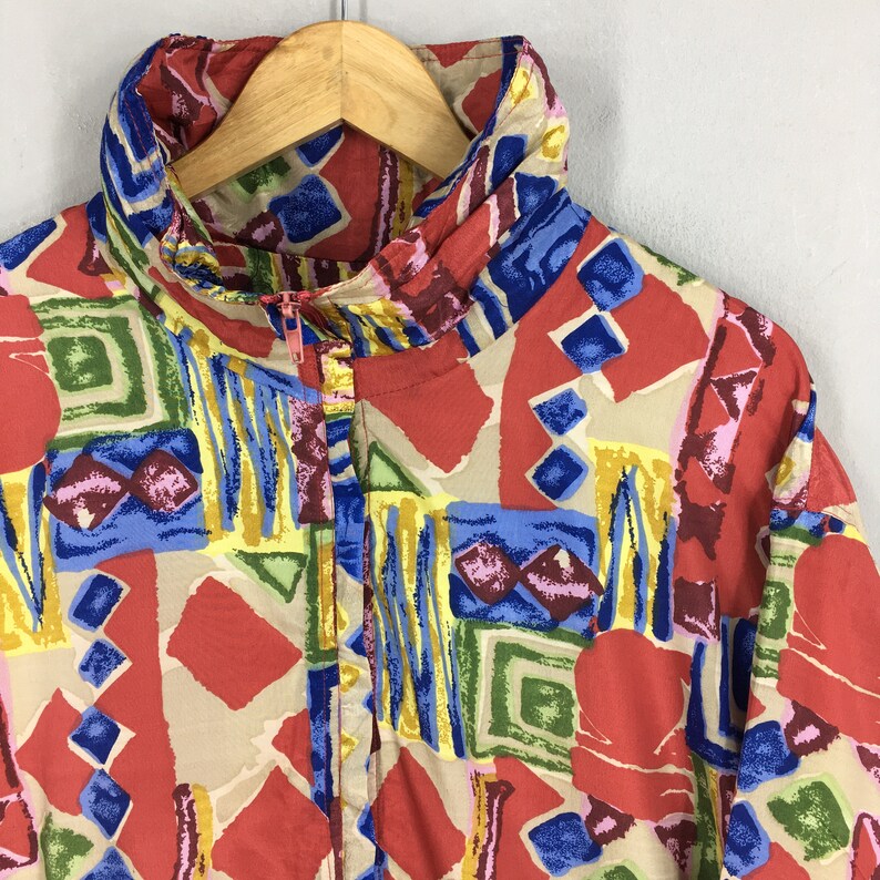 May include: A red, blue, yellow, and green patterned shirt with a zipper closure. The shirt has a stand-up collar.