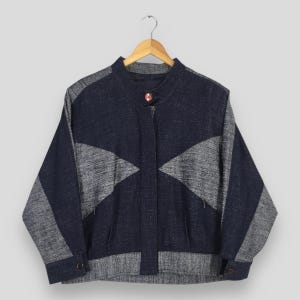 May include: A long-sleeve jacket featuring a color-blocked design in dark navy blue and heathered gray. The jacket has a mandarin collar with a single button closure, a front placket, and buttoned cuffs. The gray panels form triangular shapes.