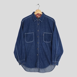 May include: A long-sleeved denim shirt with two front pockets and white stitching. The shirt has a button-down front and cuffs. The inside collar features a patterned fabric. The shirt is hanging on a wooden hanger.
