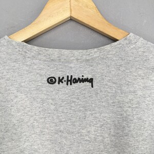 May include: A gray t-shirt with a black print of the text "&copy; K. Haring" on the back.